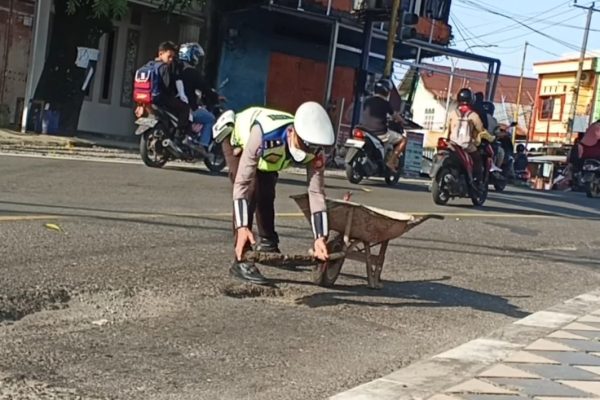 Aipda Herman, seorang anggota polisi berseragam dinas tampak mendorong gerobak berisi tanah dan sisa aspal