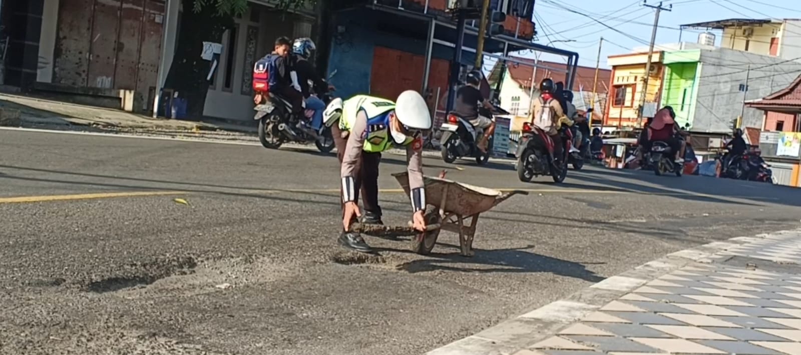 Aipda Herman, seorang anggota polisi berseragam dinas tampak mendorong gerobak berisi tanah dan sisa aspal